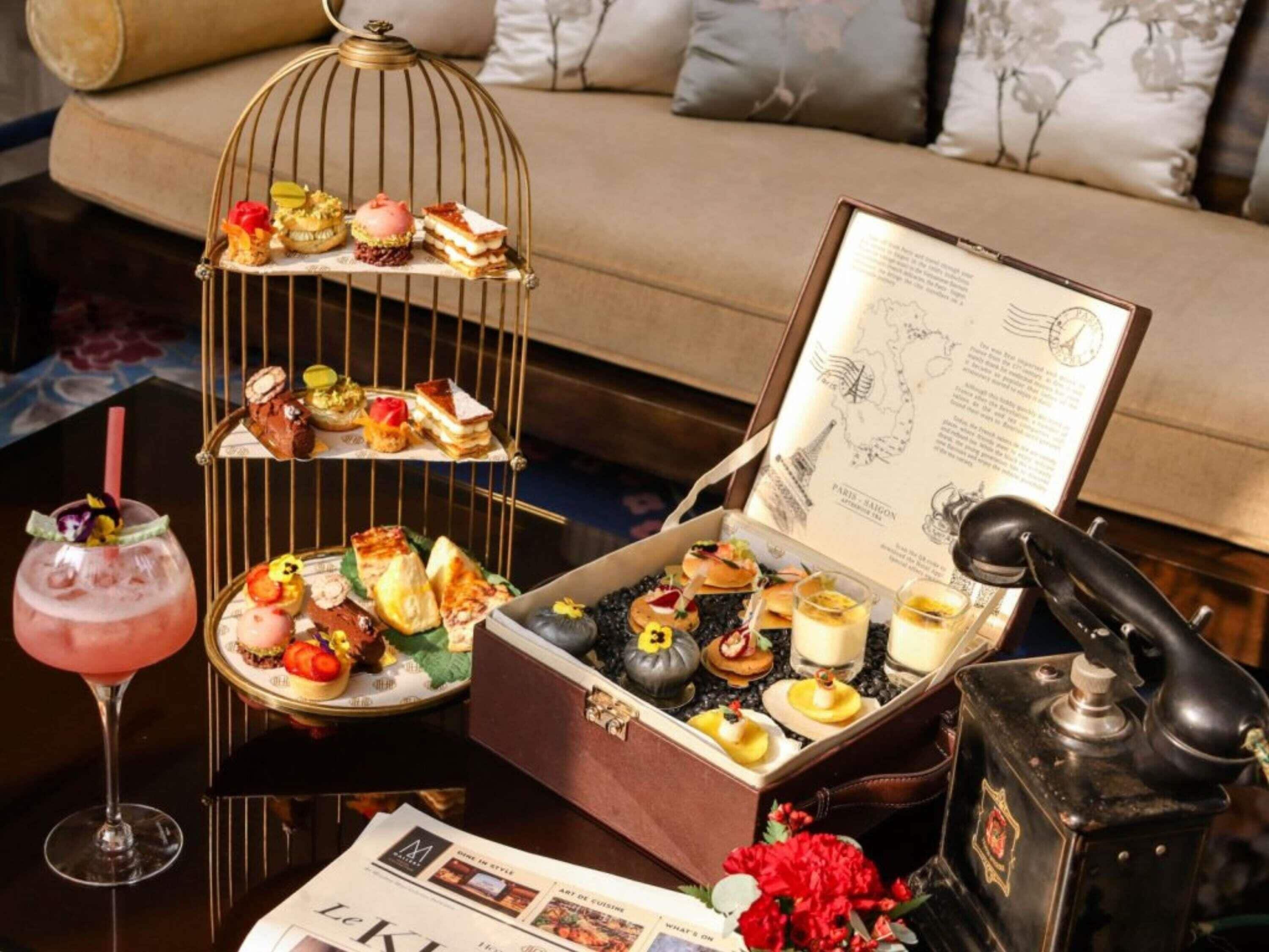 A dining setup with a three-tiered dessert stand, a cocktail, a menu, and a vintage telephone.