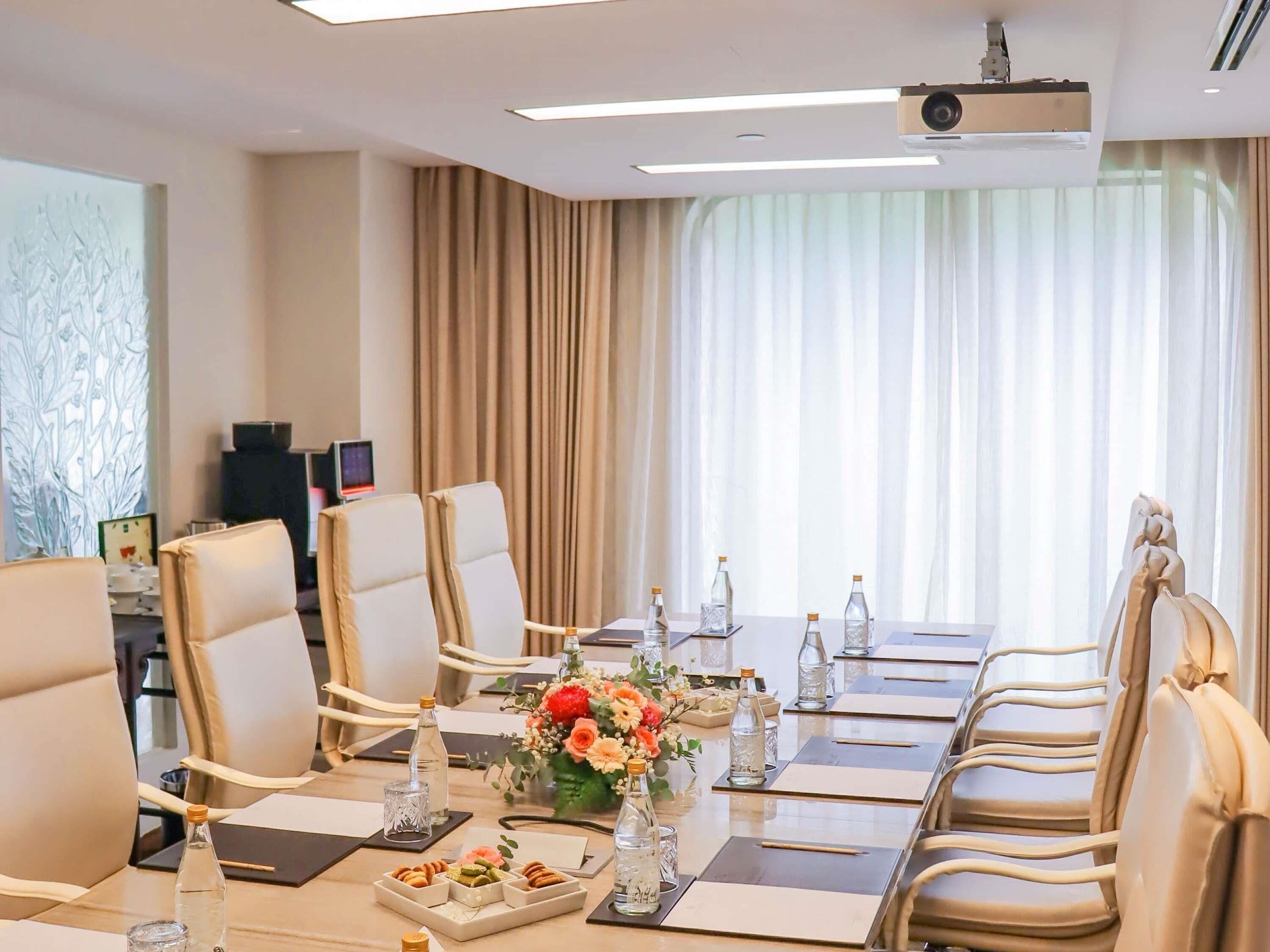 A conference room with a long table, chairs, a projector, and a large window with curtains.