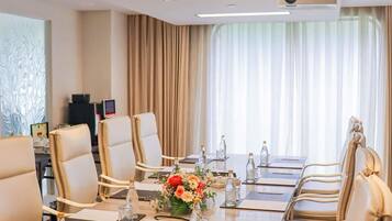 A conference room with a long table, chairs, a projector, and a large window with curtains.