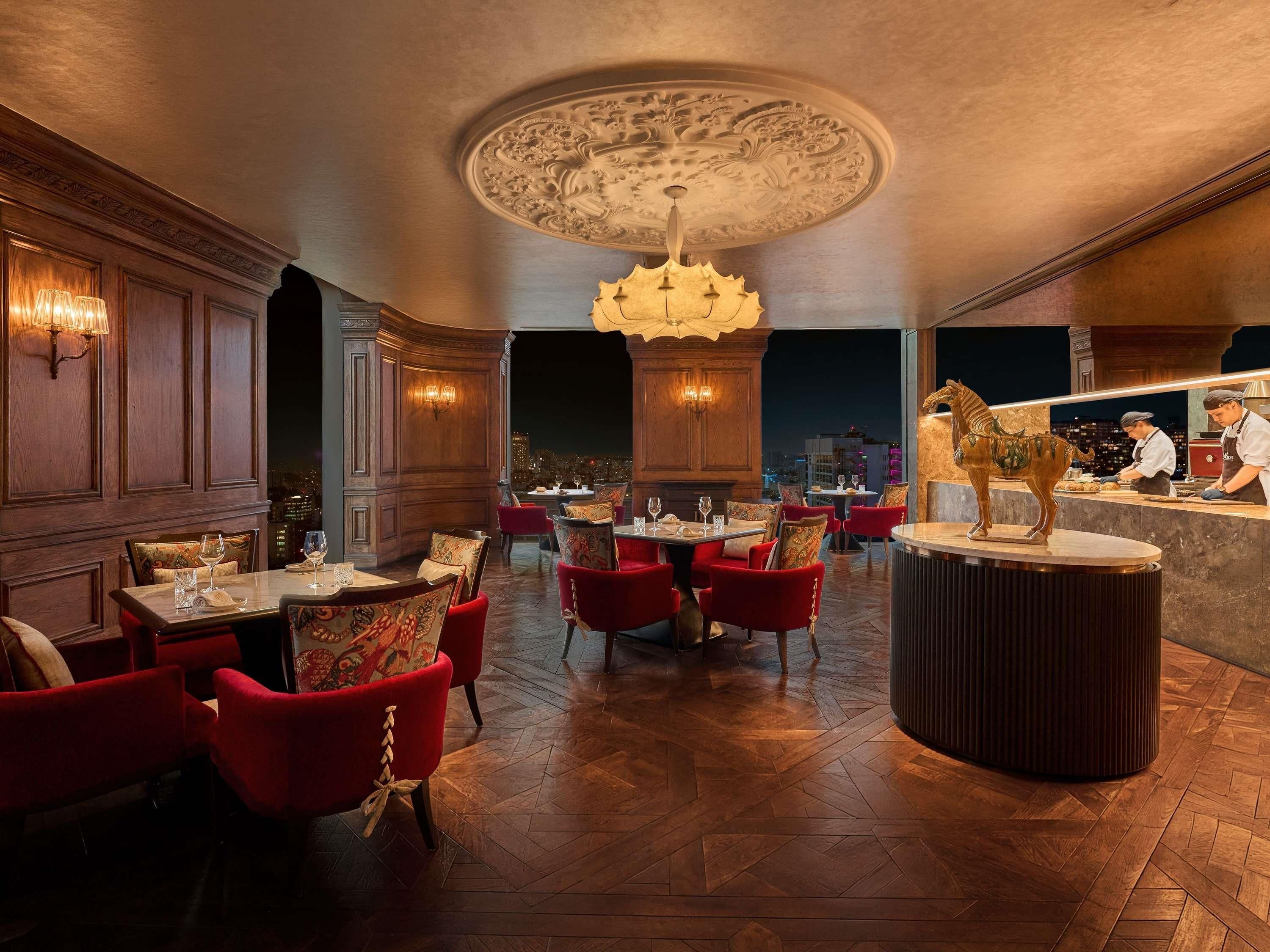 A restaurant with a high ceiling, ornate ceiling design, and a view of the city at night.