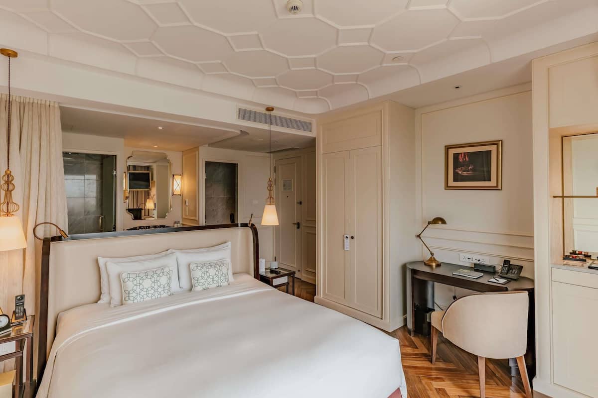 A hotel room with a large bed, a desk, a chair, and a mirror.