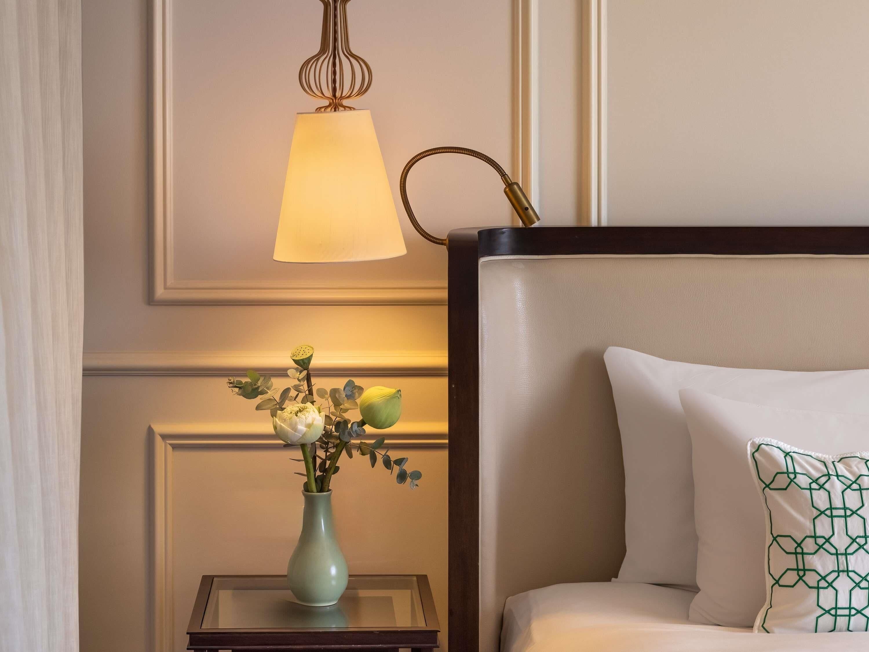 A hotel room with a bed, a nightstand with a vase of flowers, and a hanging lamp.