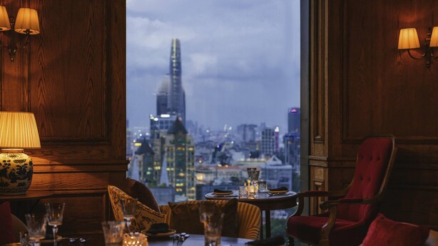 Un coin repas avec une table dressée pour deux personnes, une vue sur la ville et des lambris en bois.