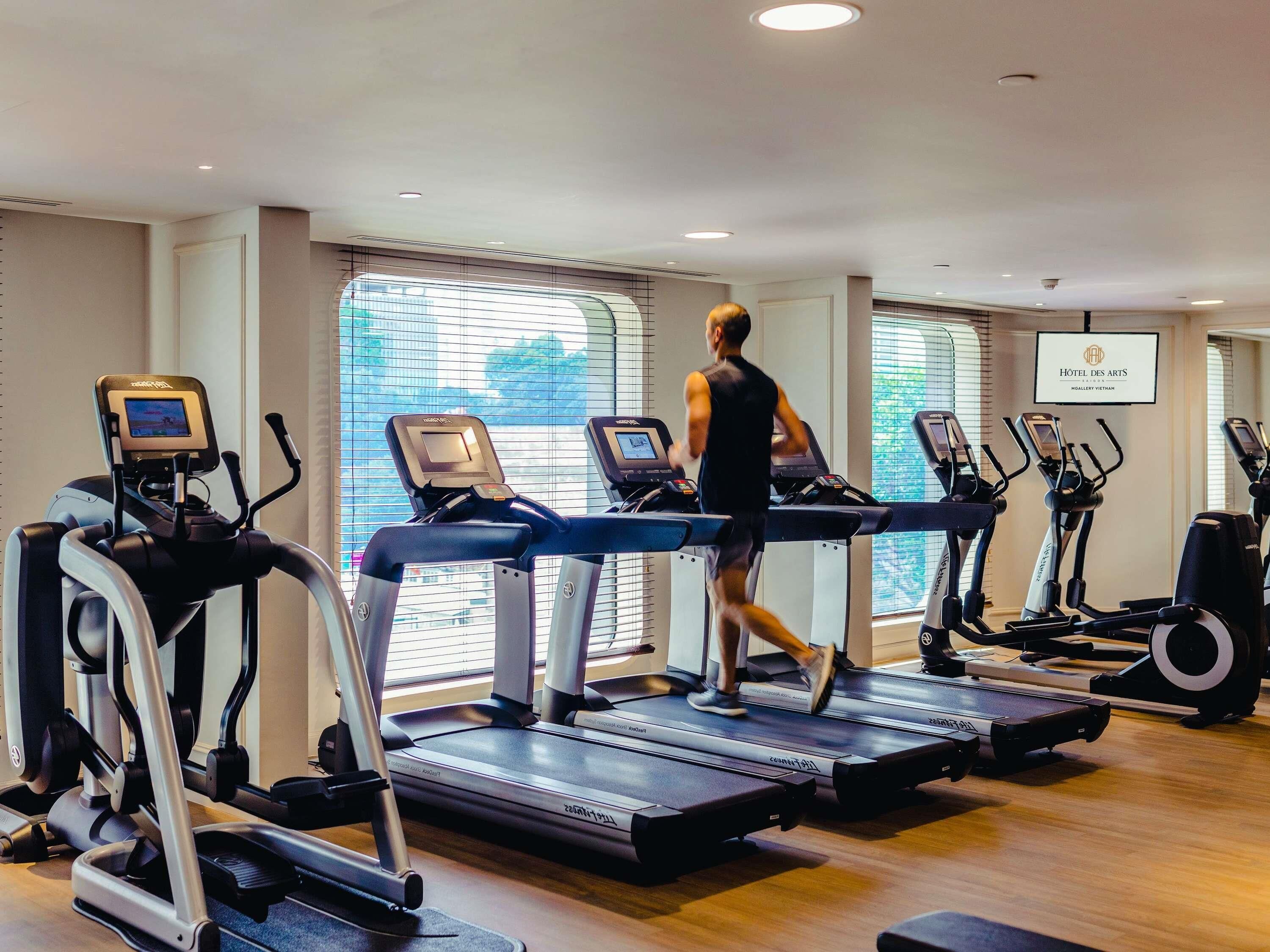 A gym with treadmills, ellipticals, and a person running.
