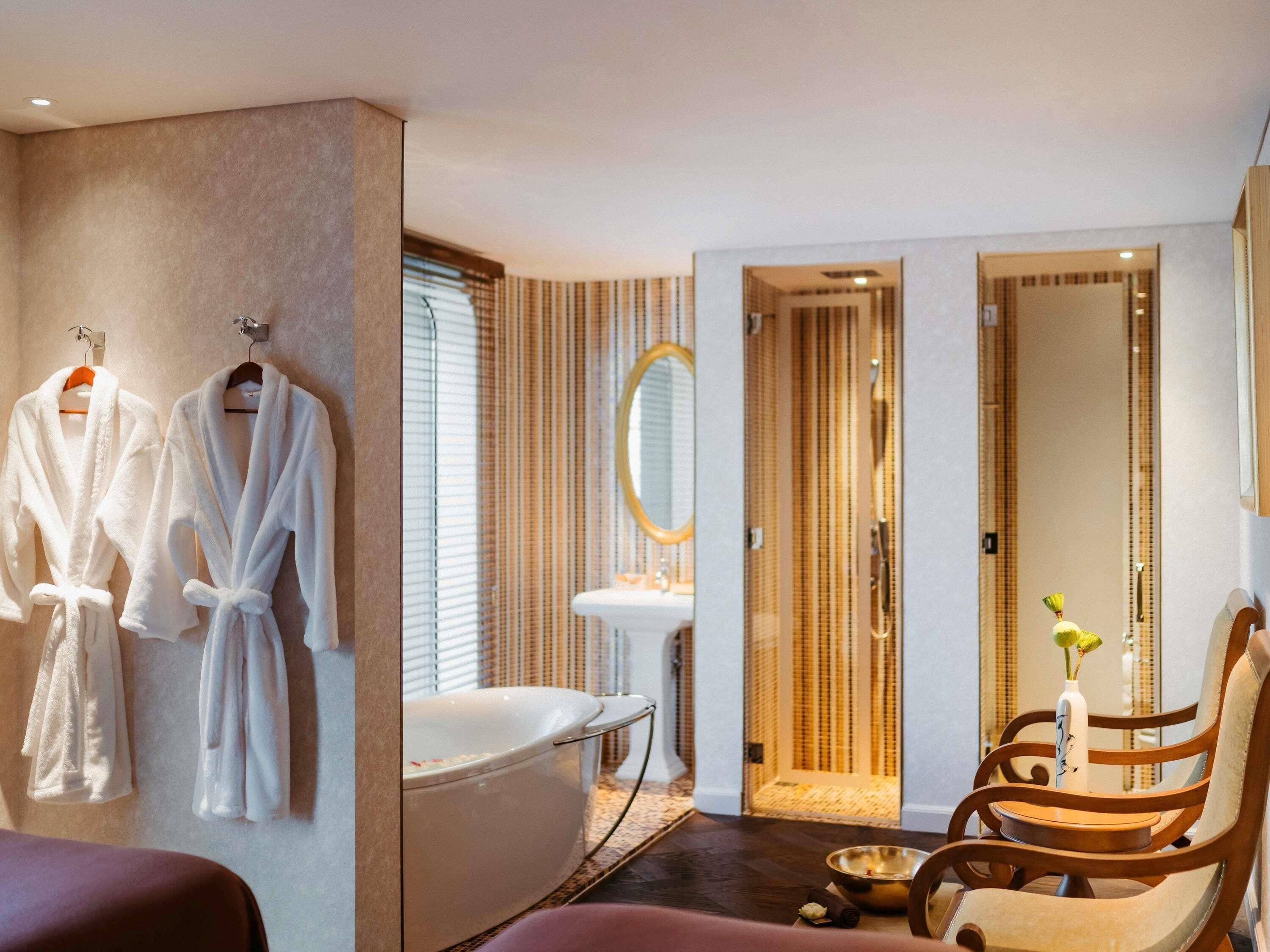 Une salle de bain moderne avec une baignoire, un miroir et deux peignoirs blancs accrochés au mur.