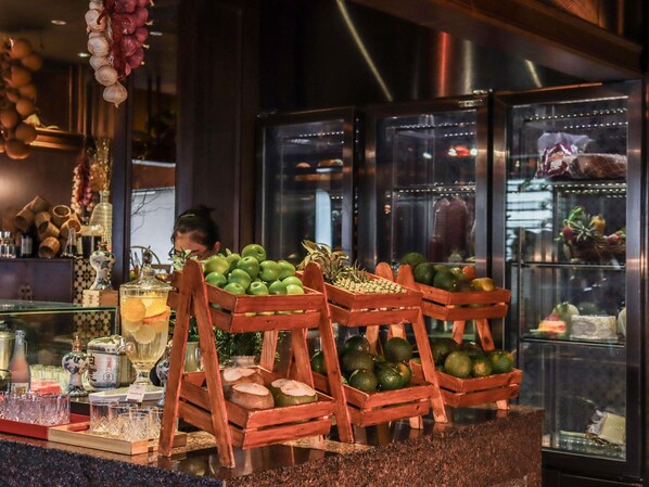 Une présentation de produits frais, notamment des pommes vertes et des citrons verts dans des caisses en bois, une vitrine contenant divers articles, et une personne à l’arrière-plan.