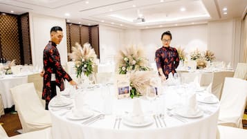 Un salón de banquetes con mesas redondas dispuestas para un evento formal, con manteles blancos, centros de mesa florales y tarjetas de nombres.