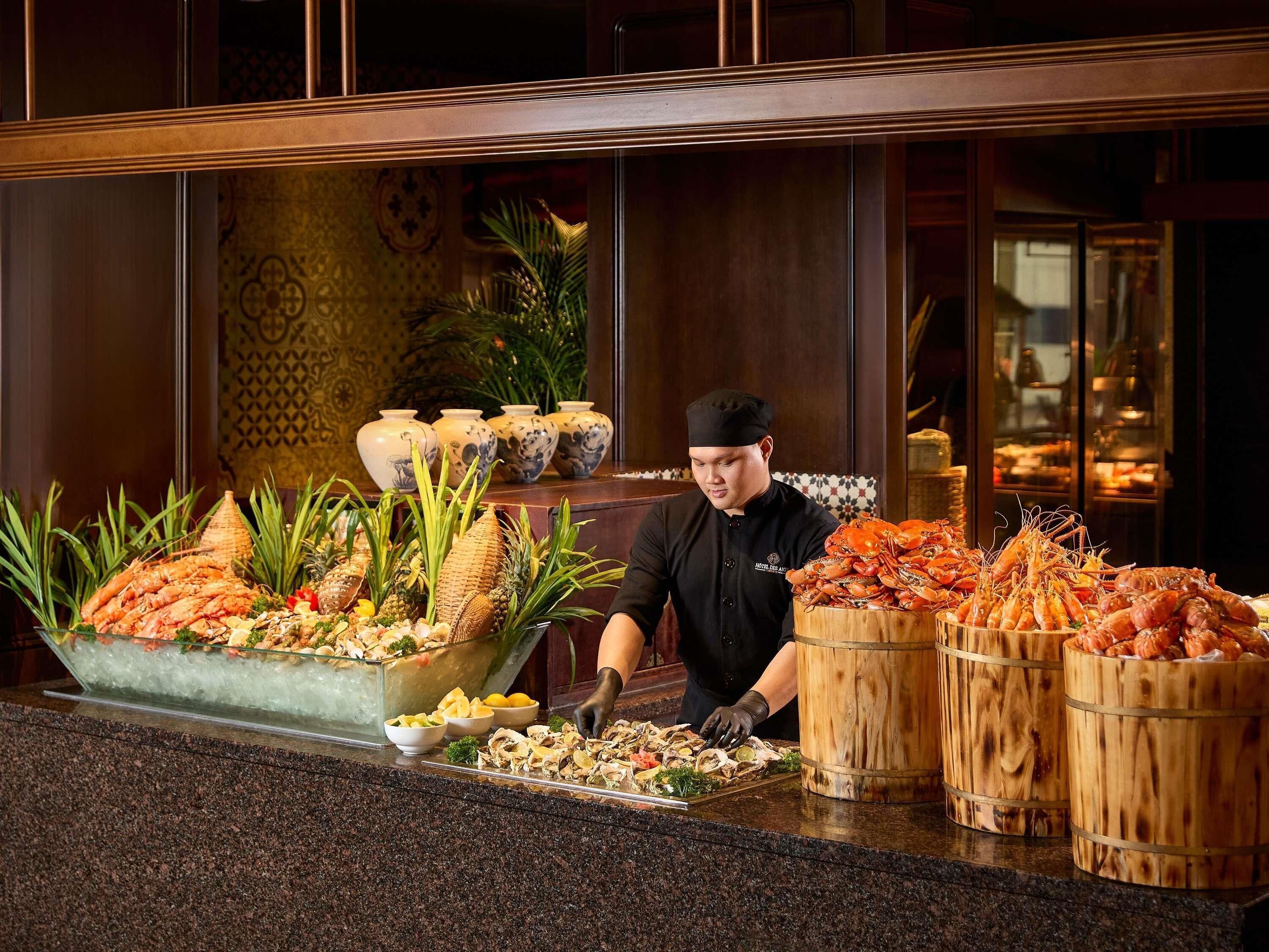 Ein Koch an einem Buffet mit Meeresfrüchten, tropischen Früchten und dekorativen Vasen.