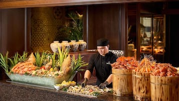 A chef at a buffet with seafood, tropical fruits, and decorative vases.