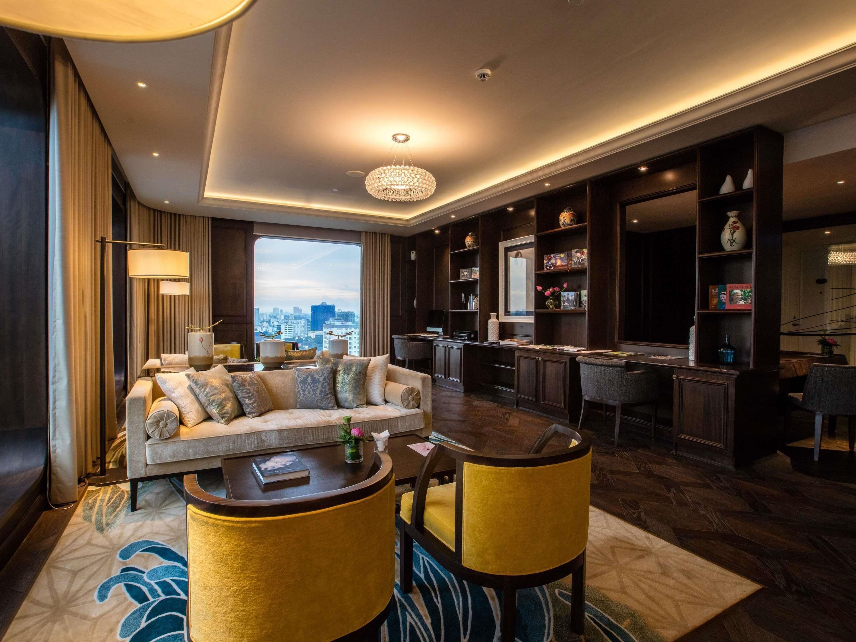 A modern living room with a sofa, chairs, a coffee table, a bookshelf, and a city view.