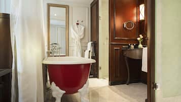 A bathroom with a red clawfoot bathtub, a white sink, a mirror, and a wooden door.