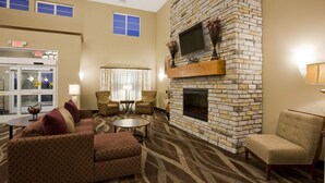 A hotel lobby with a stone fireplace, comfortable seating, and a television mounted on the wall. - Gateway Park Hotel and Suites (Tea)