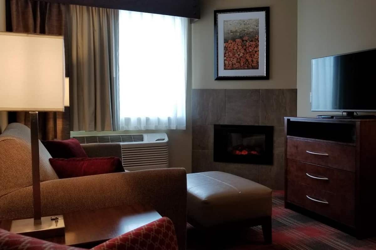 Ein Hotelzimmer mit Sofa, Hocker, Fernseher, Kamin und Lampe.