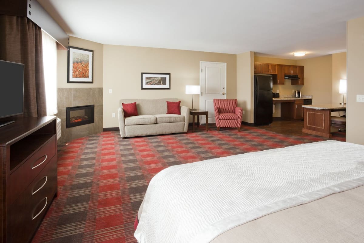 Ein Hotelzimmer mit einem großen Bett, einer Couch, einem Sessel, einem Fernseher, einem Kamin und einer Küchenzeile.