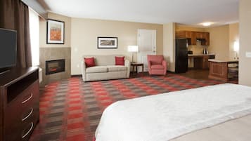 Een hotelkamer met een groot bed, een bank, een fauteuil, een televisie, een open haard en een kitchenette.