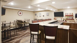 A bar area with a counter, bar stools, and a selection of bottles on shelves. - Gateway Park Hotel and Suites (Tea)