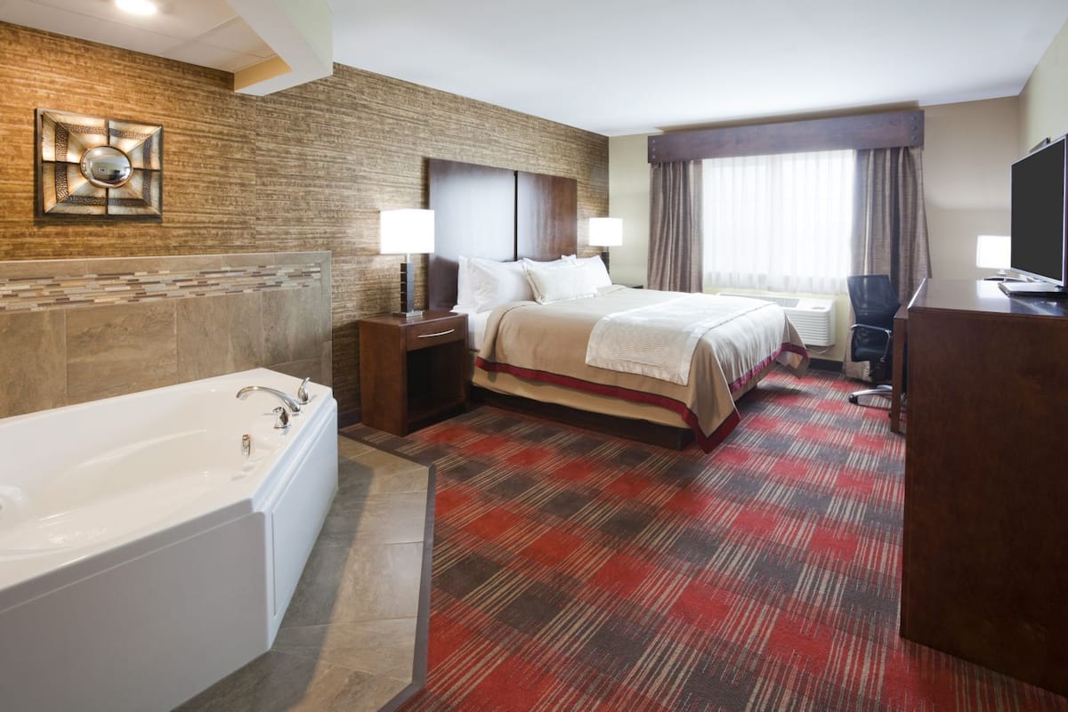 Ein Hotelzimmer mit einem großen Bett, einem separaten Badezimmer mit Badewanne und einem Schreibtisch mit Fernseher.