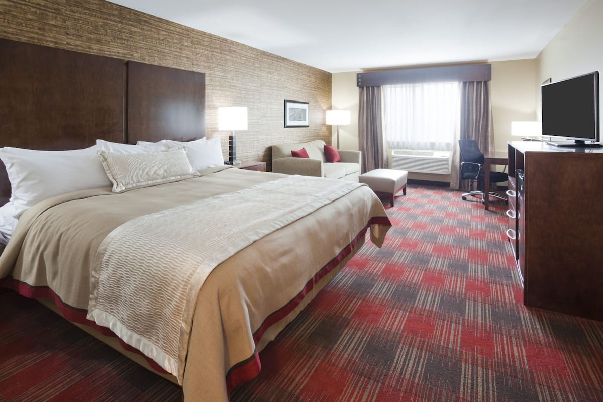 Ein Hotelzimmer mit einem großen Bett, einem Schreibtisch, einem Sessel und einem Fernseher.