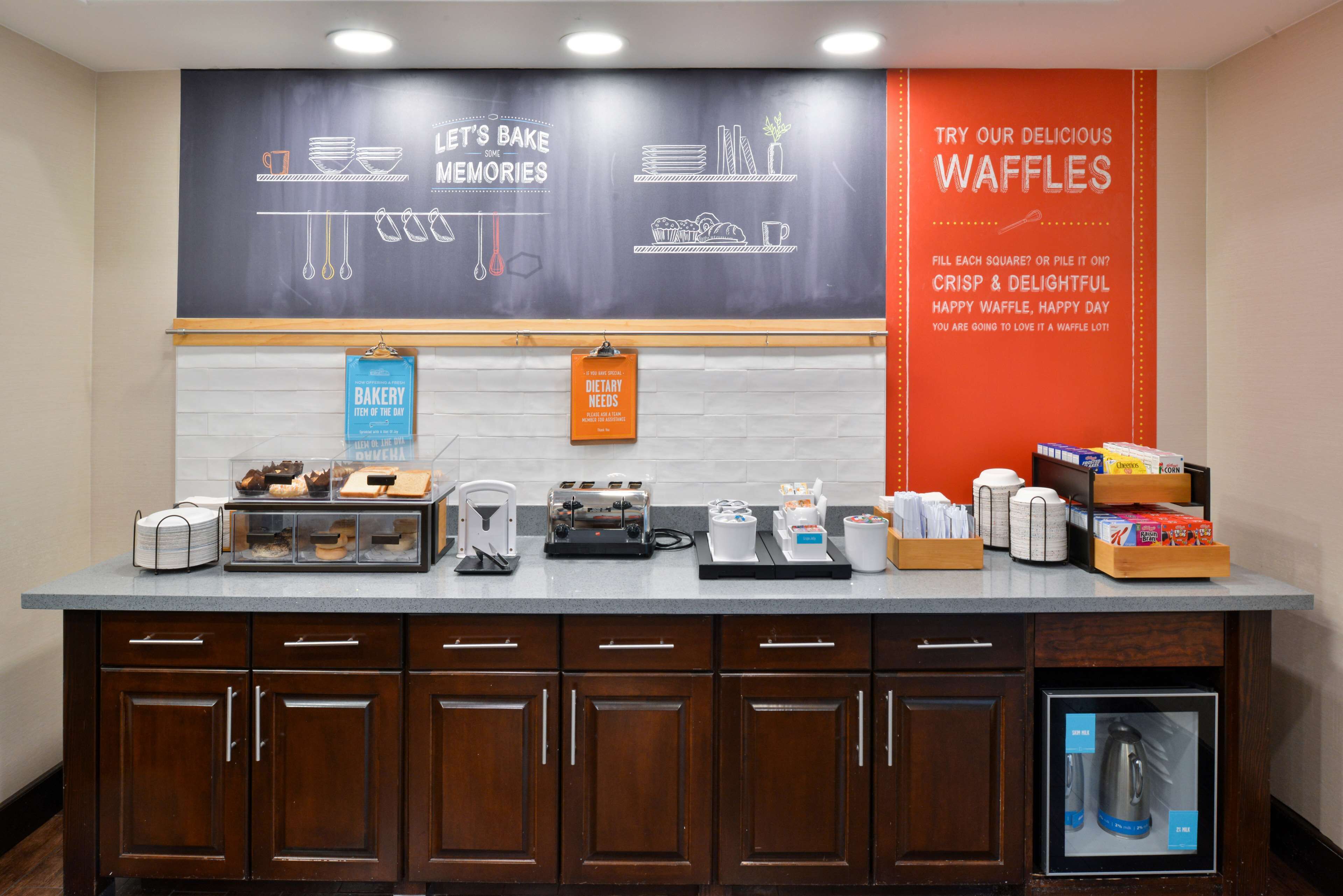 A bakery counter with various baking tools and ingredients, a chalkboard with baking tips, and a sign promoting waffles.
