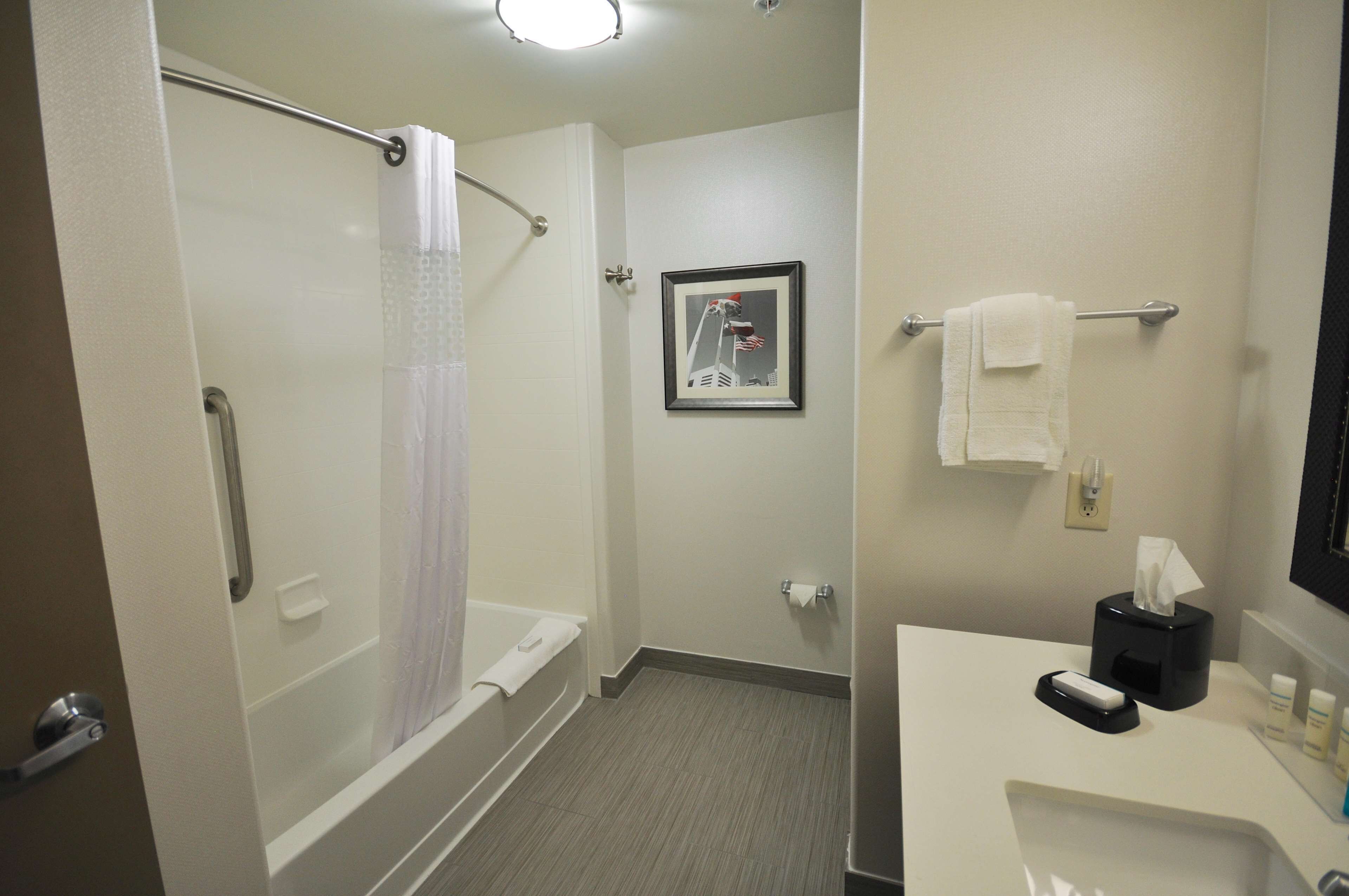 A bathroom with a shower, toilet, sink, and a framed picture on the wall.