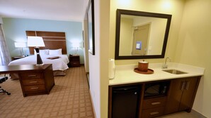A hotel room with a bed, bedside tables, a desk, a mirror, a sink, and a compact dishwasher. - Hampton Inn & Suites Hutto Austin (Hutto)