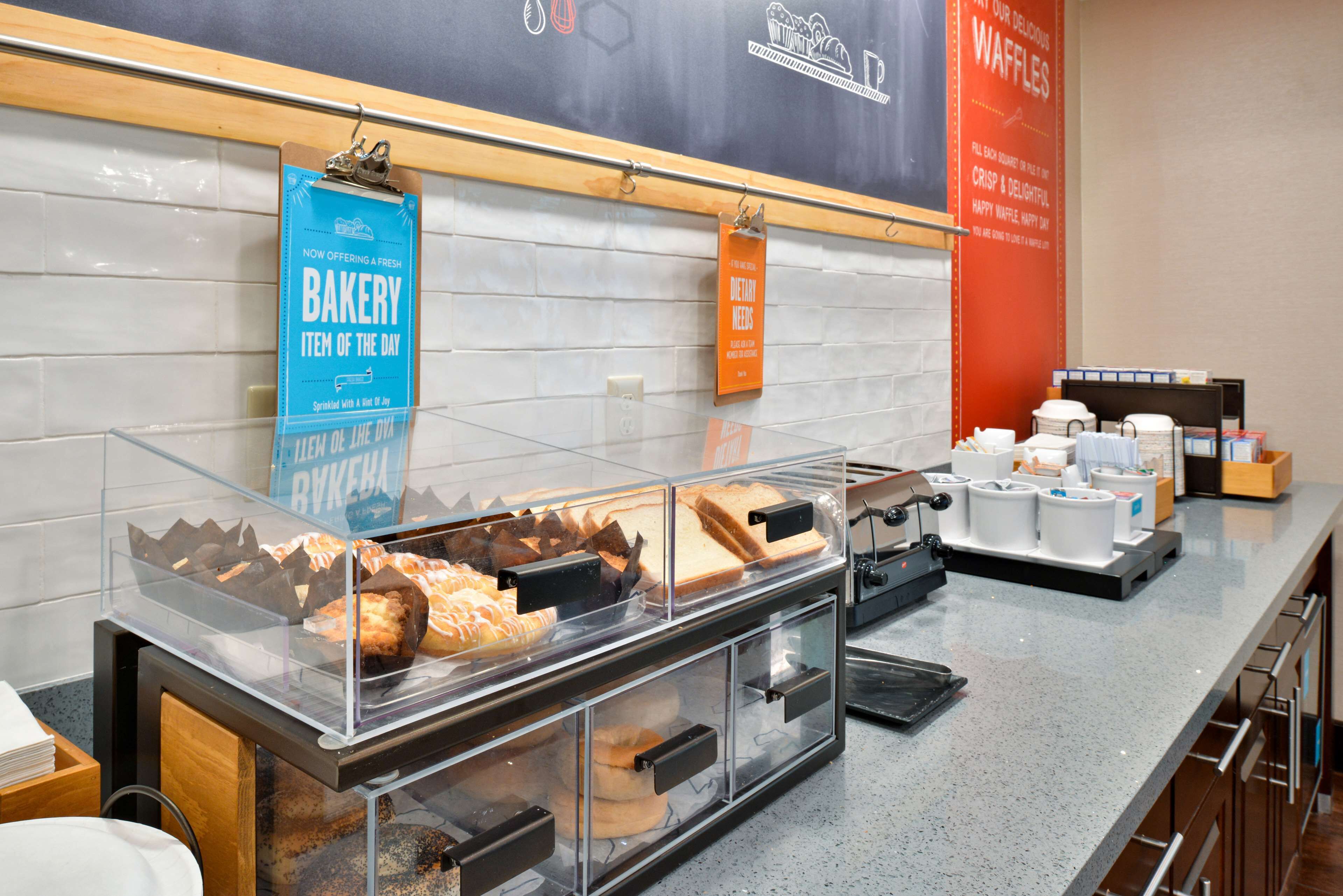 A bakery display with various baked goods and a sign indicating a bakery item of the day.