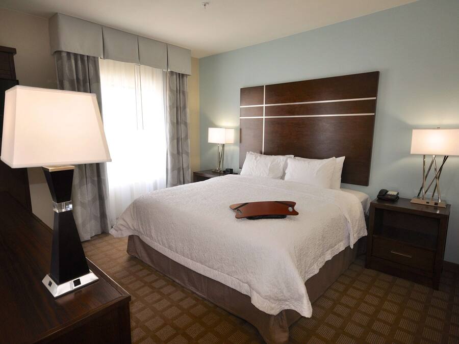 Habitación de hotel con una cama grande, dos mesitas de noche con lámparas, un cabecero de madera y una alfombra estampada.