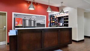 A hotel reception desk with a red wall, a framed advertisement, and a minibar. - Hampton Inn & Suites Hutto Austin (Hutto)