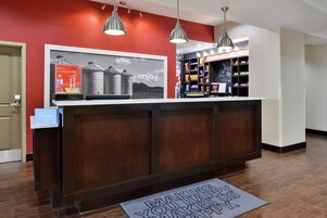 Un mostrador de recepción de hotel con una pared roja, un anuncio enmarcado y un minibar.