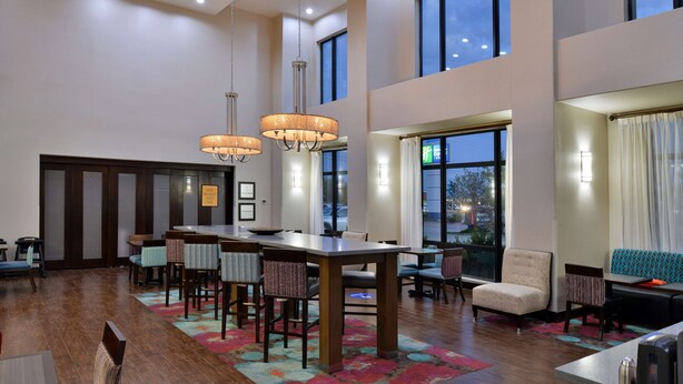 A spacious hotel lobby with a large dining table, multiple chairs, and a seating area with sofas and armchairs. - Hampton Inn & Suites Hutto Austin (Hutto)