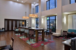 Un hall de hotel espacioso con una gran mesa de comedor, múltiples sillas y una zona de estar con sofás y sillones.