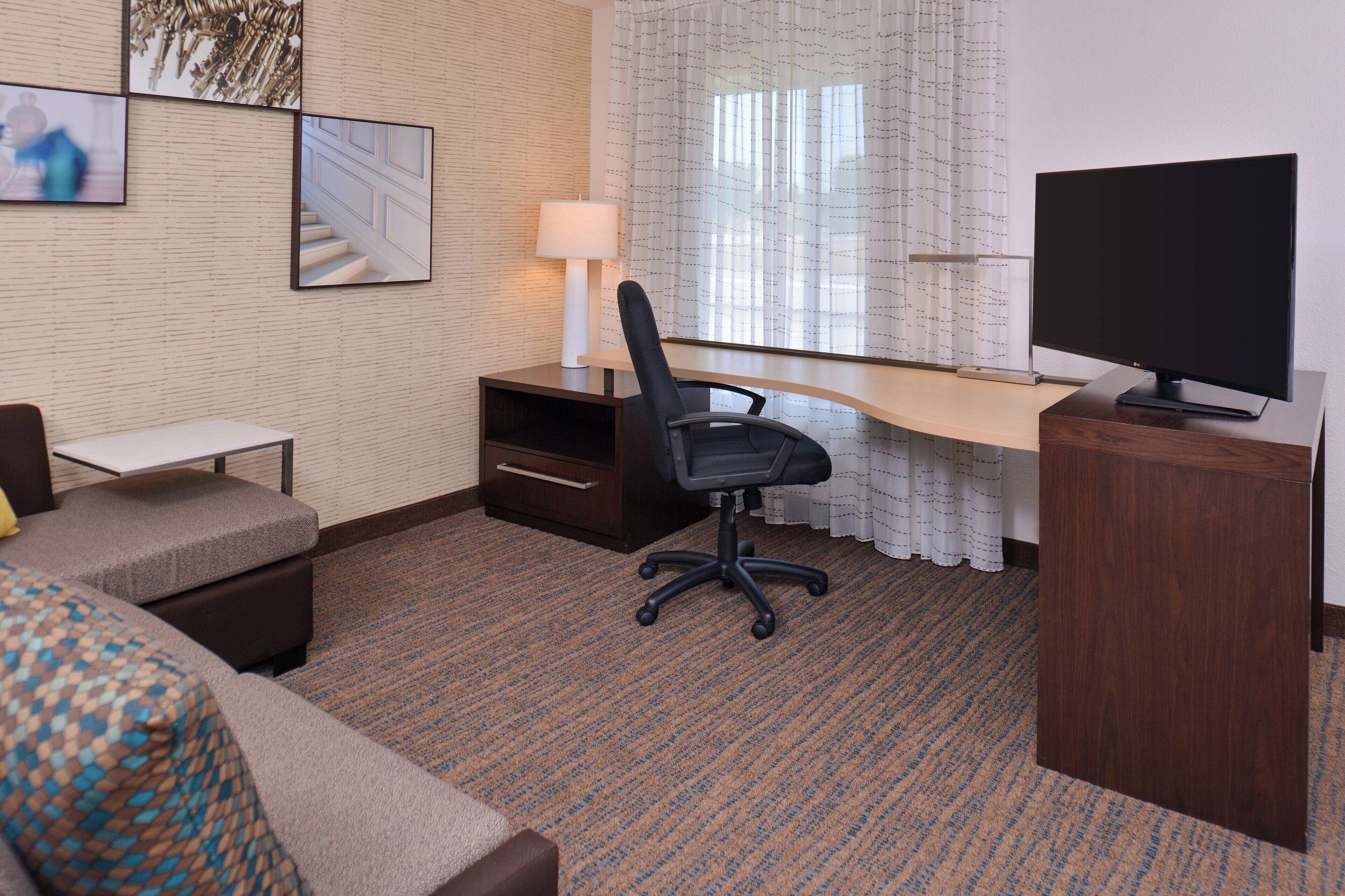 A hotel room with a desk, chair, television, and a bed.