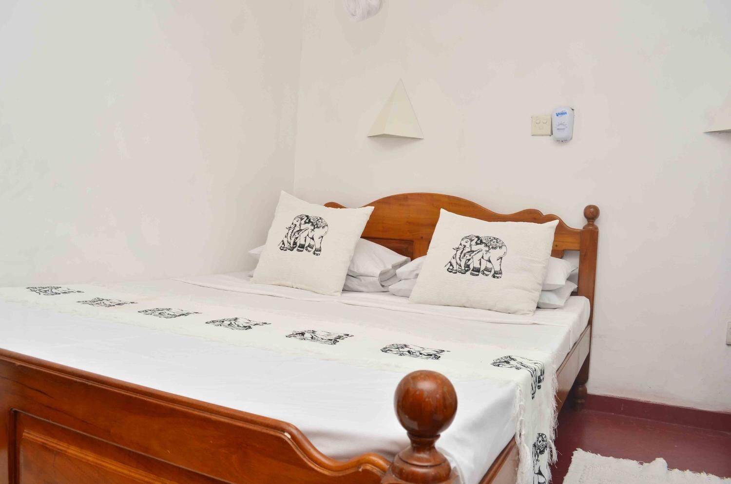 A bed with a wooden headboard, white bedding, and decorative pillows with elephant designs.