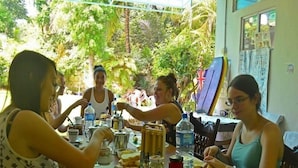 A group of people dining at an outdoor table with various dishes, cups, and condiments.