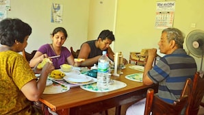 A group of people dining at a wooden table with plates, bowls, and a water bottle.
