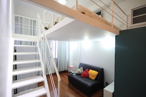 A room with a bunk bed, a black sofa with colorful cushions, and a small table with books.