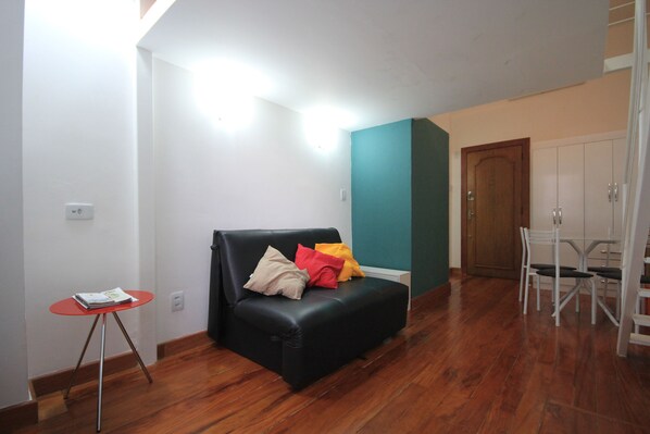 Un salon avec un canapé noir, une petite table rouge et un mur d’accent de couleur turquoise.