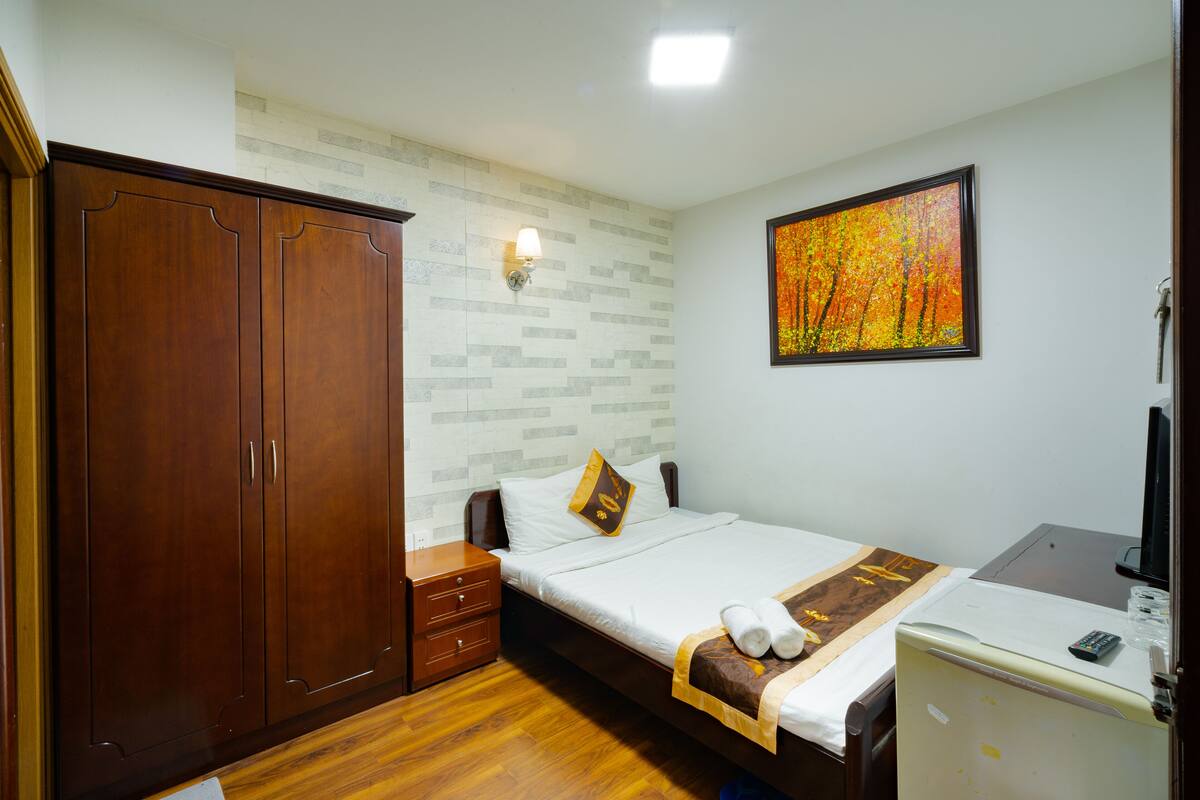 Ein Schlafzimmer mit Bett, Kleiderschrank, Schreibtisch mit Computer, Wand-Fernseher und einem Gemälde.
