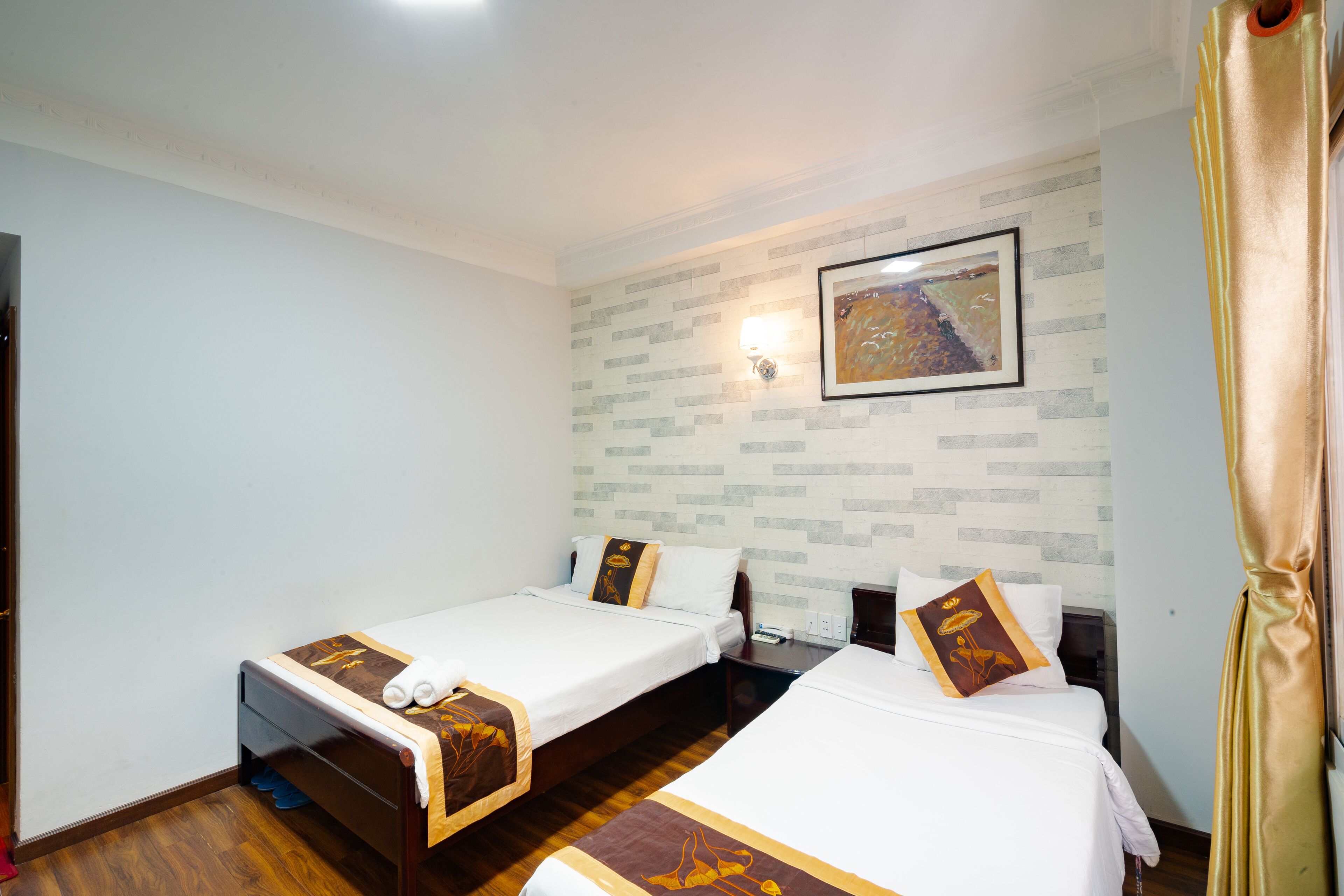 A hotel room with two single beds, a nightstand, a wall-mounted light, and a painting.