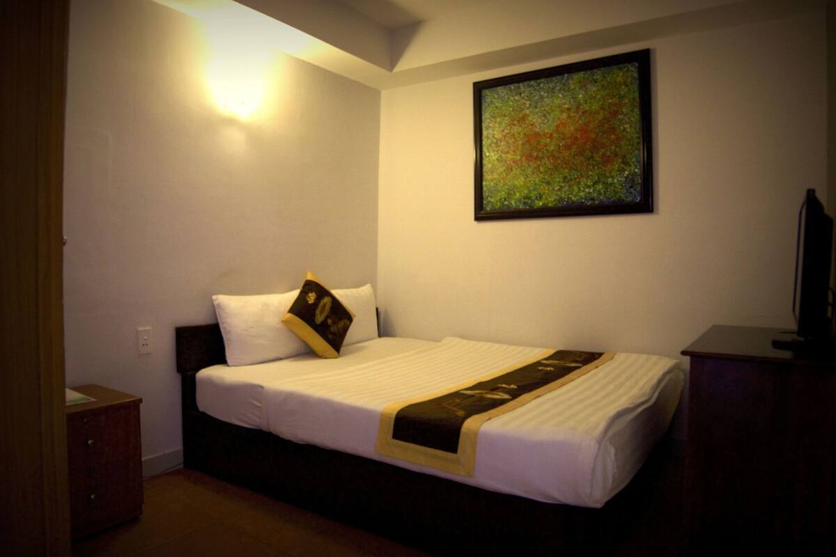 Ein Hotelzimmer mit einem Bett, einem Nachttisch, einer Lampe und einem Gemälde an der Wand.