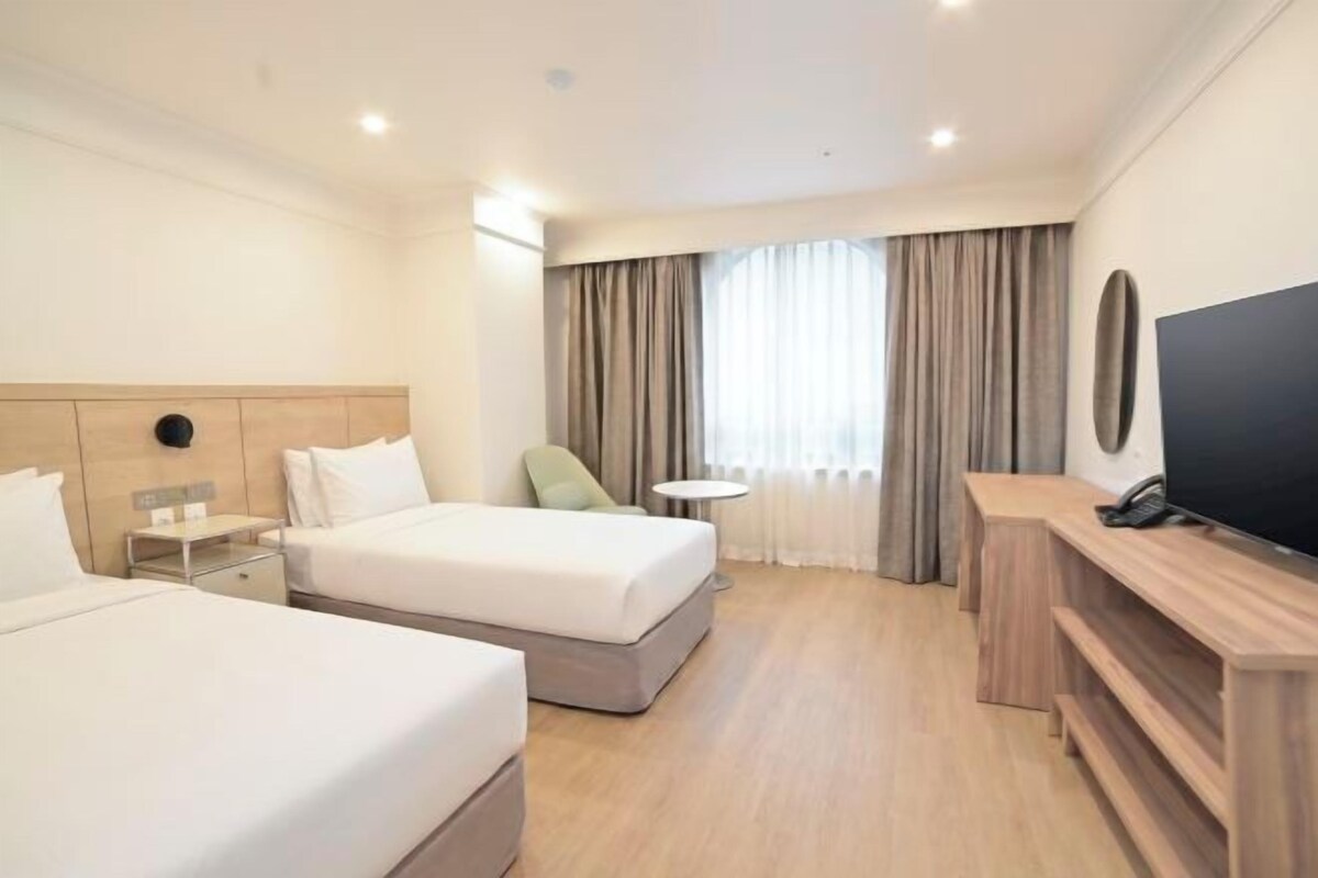 A hotel room with two beds, a TV, a small table, and a desk.