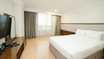 A hotel room with a bed, a TV, a desk with a phone, and a window with curtains.