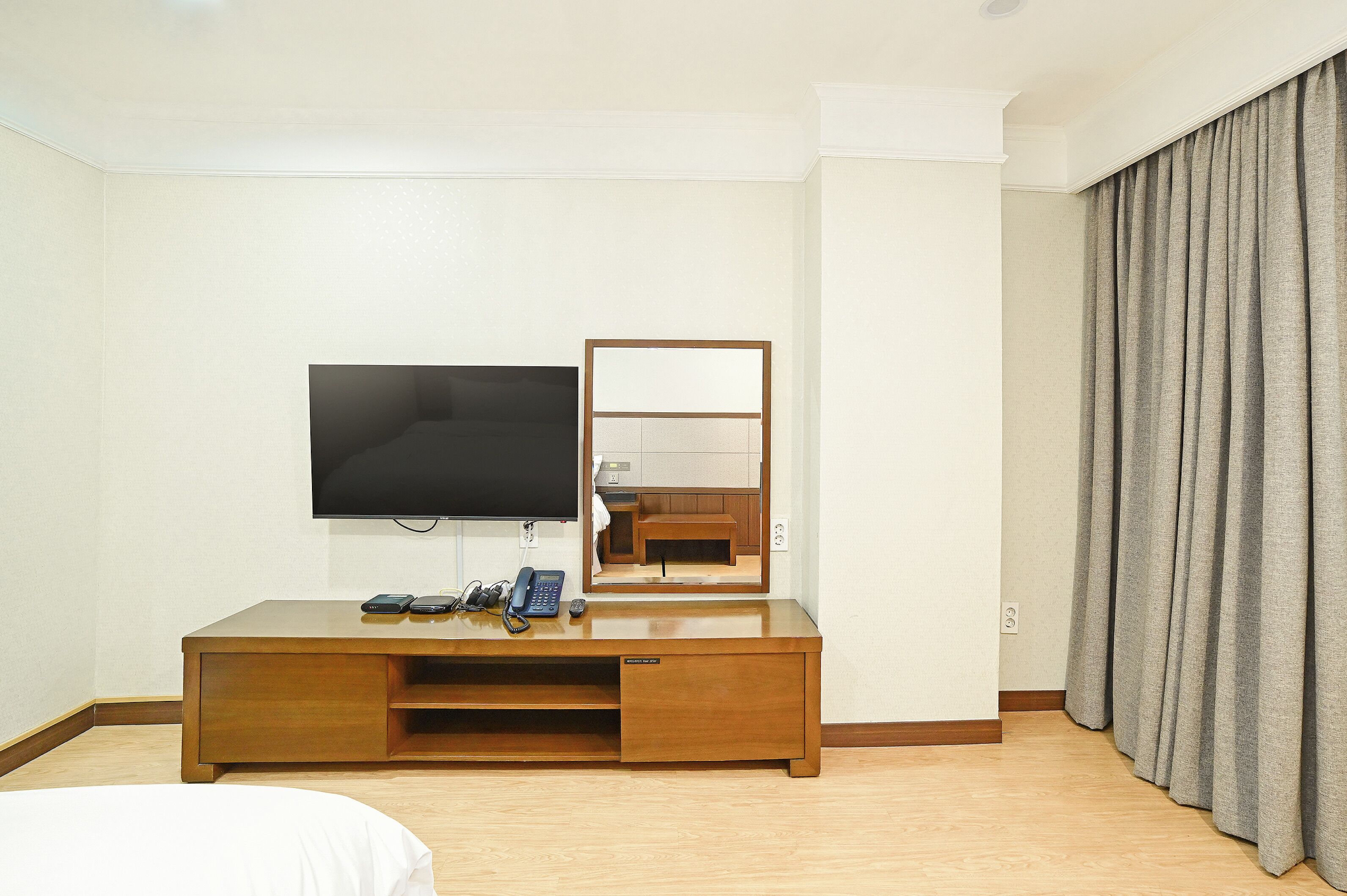 Una habitación de hotel con televisión de pantalla plana, un escritorio de madera con teléfono y un espejo.