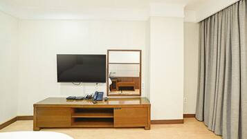 Una habitación de hotel con televisión de pantalla plana, un escritorio de madera con teléfono y un espejo.