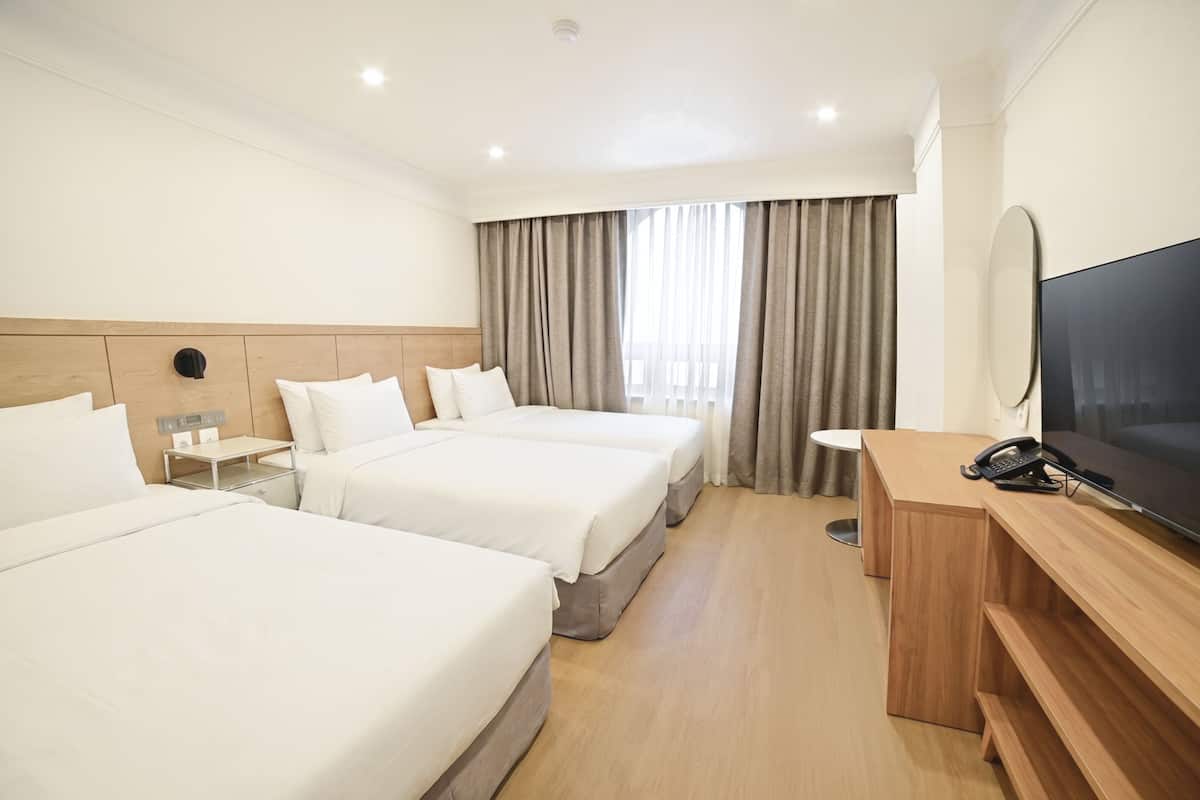 Habitación de hotel con tres camas, un escritorio, un televisor y un teléfono.