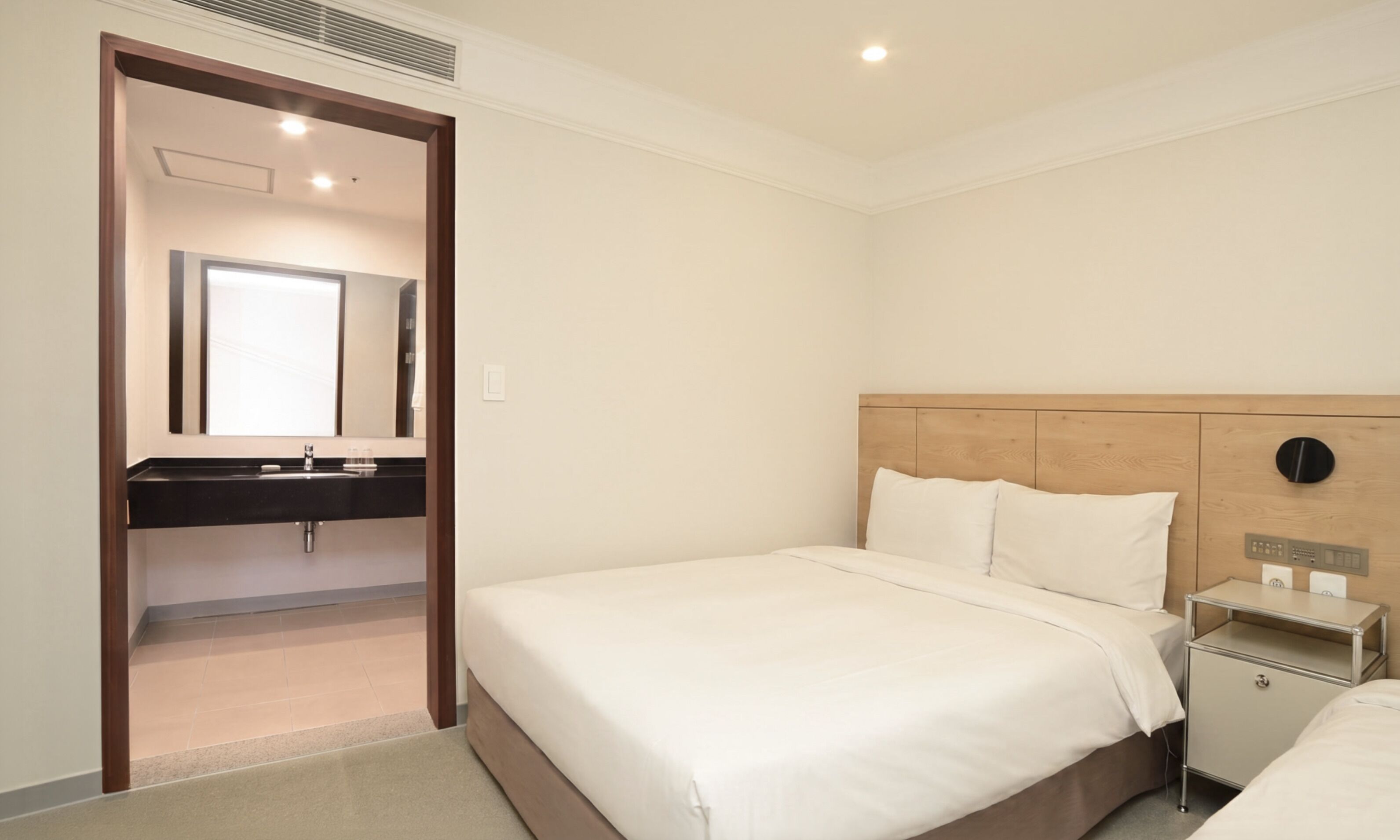 Une chambre d’hôtel comprenant un lit, une table de chevet, une commode, un miroir et une salle de bain avec un lavabo et un miroir.