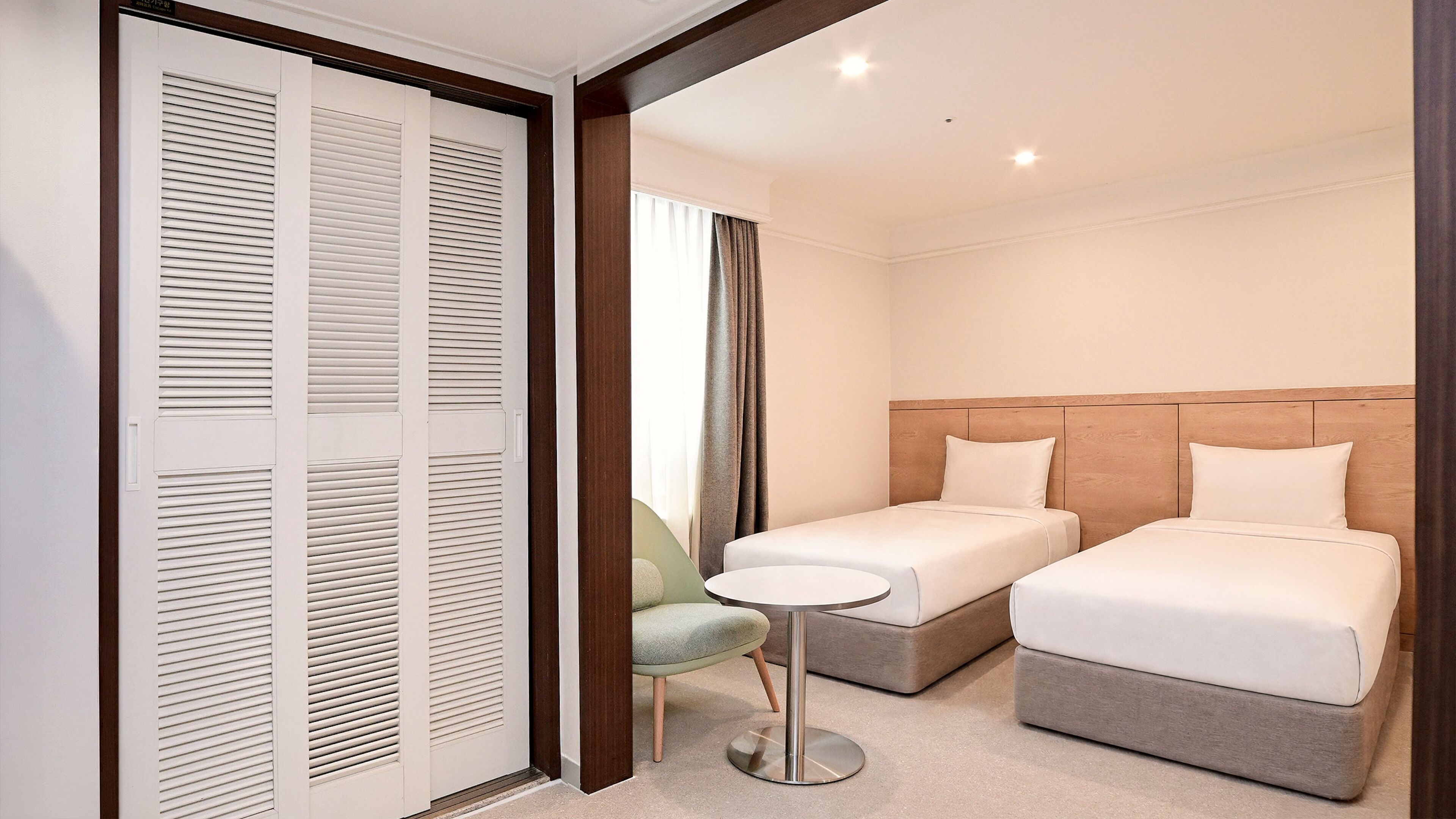 Habitación de hotel con dos camas individuales, una mesita redonda y una silla verde.