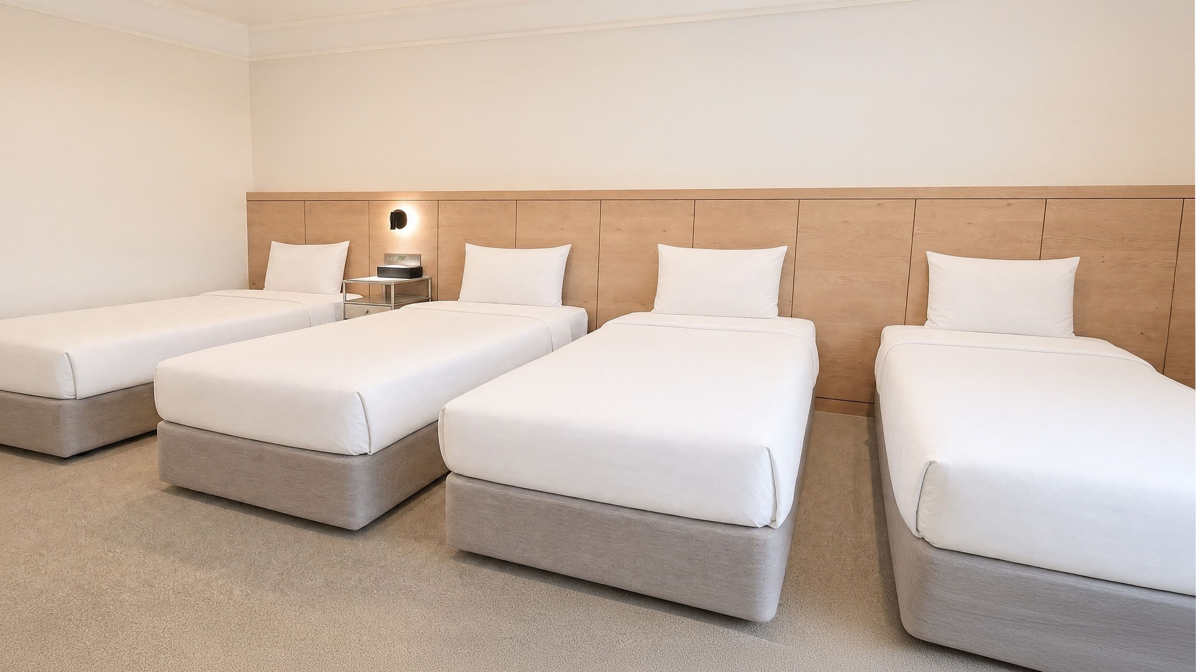 A hotel room with four single beds, a nightstand with a lamp, and a wooden headboard.