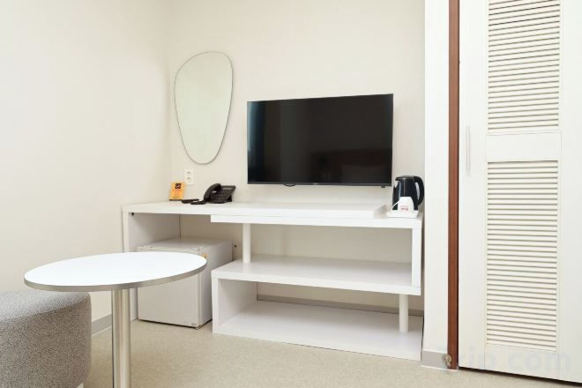 A hotel room with a bed, a bedside table, a TV, a mirror, and a wardrobe.