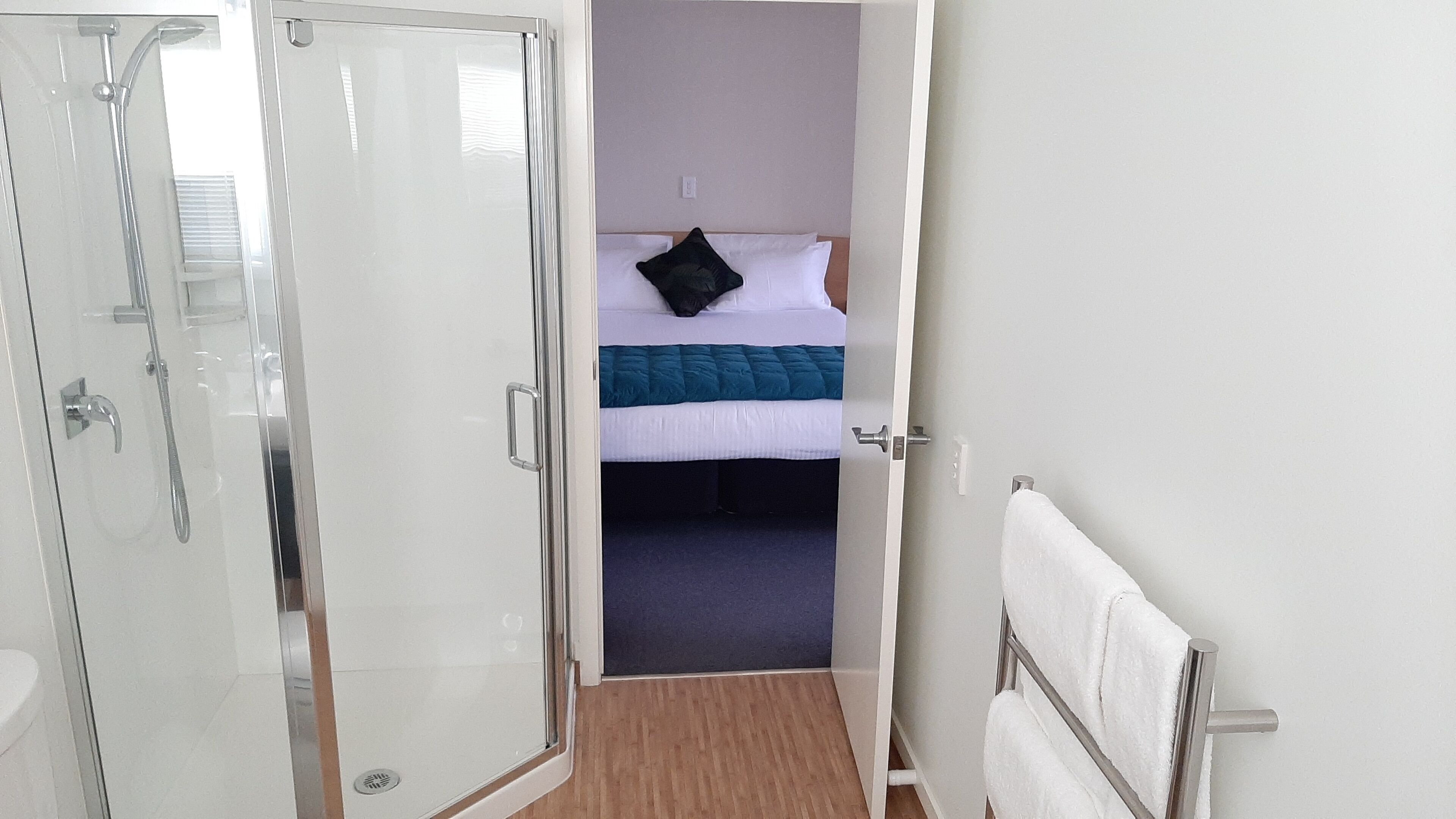 Une chambre d’hôtel avec une douche, un lit recouvert d’une couette bleue et blanche, et une serviette blanche posée sur un porte-serviettes en métal.